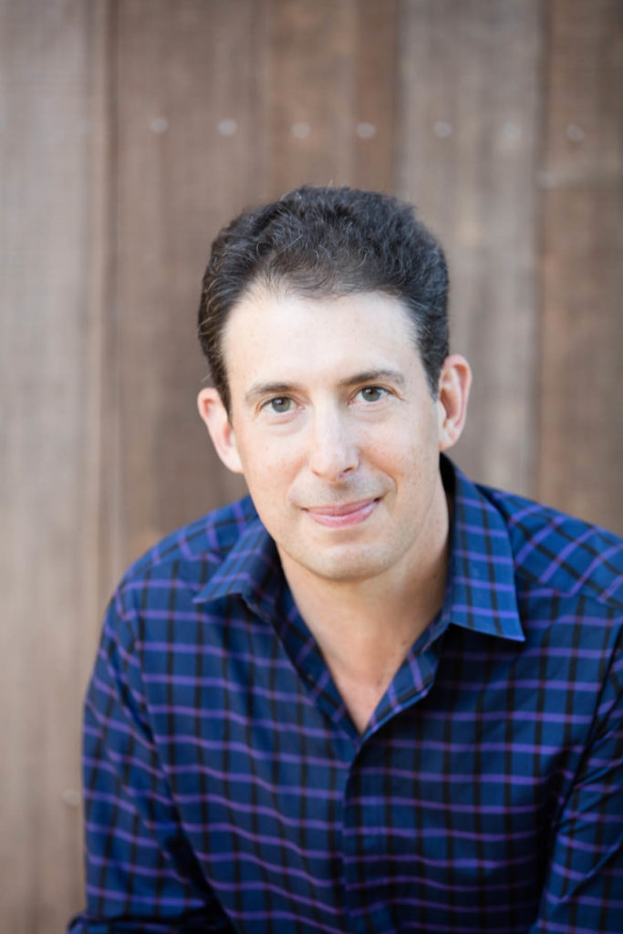 Headshot of Eric Klinenberg, who has short brown hair and wears a blue patterned shirt.