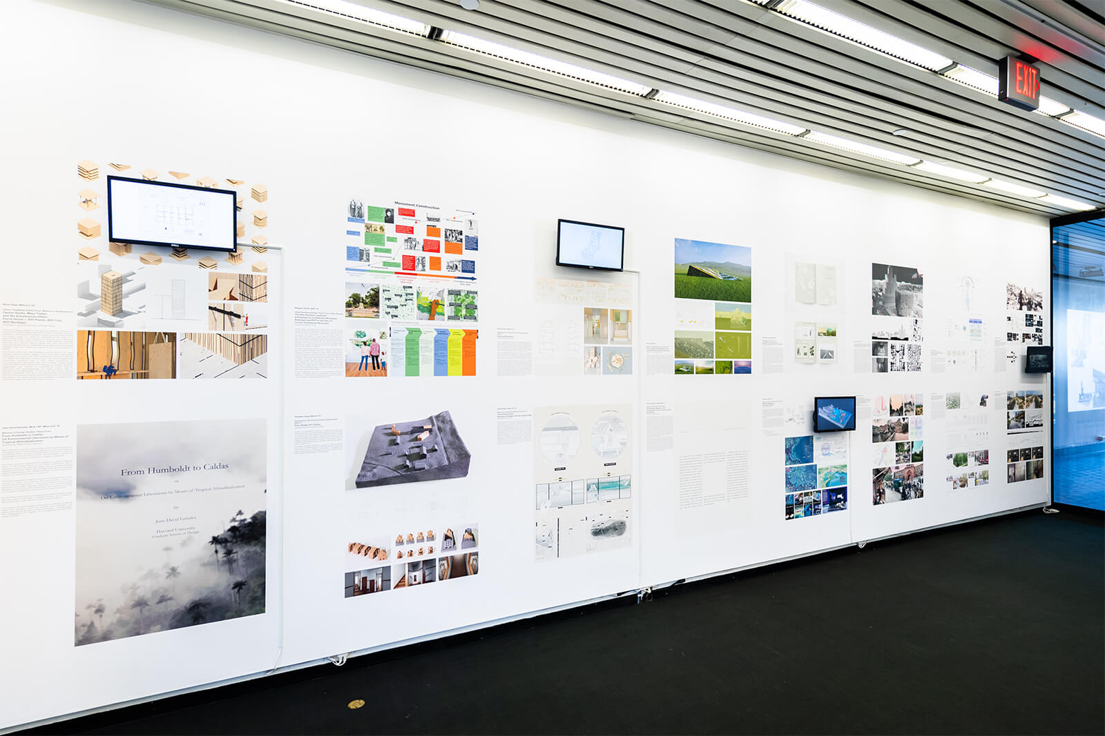 Exhibition wall with drawings and multimedia screens.