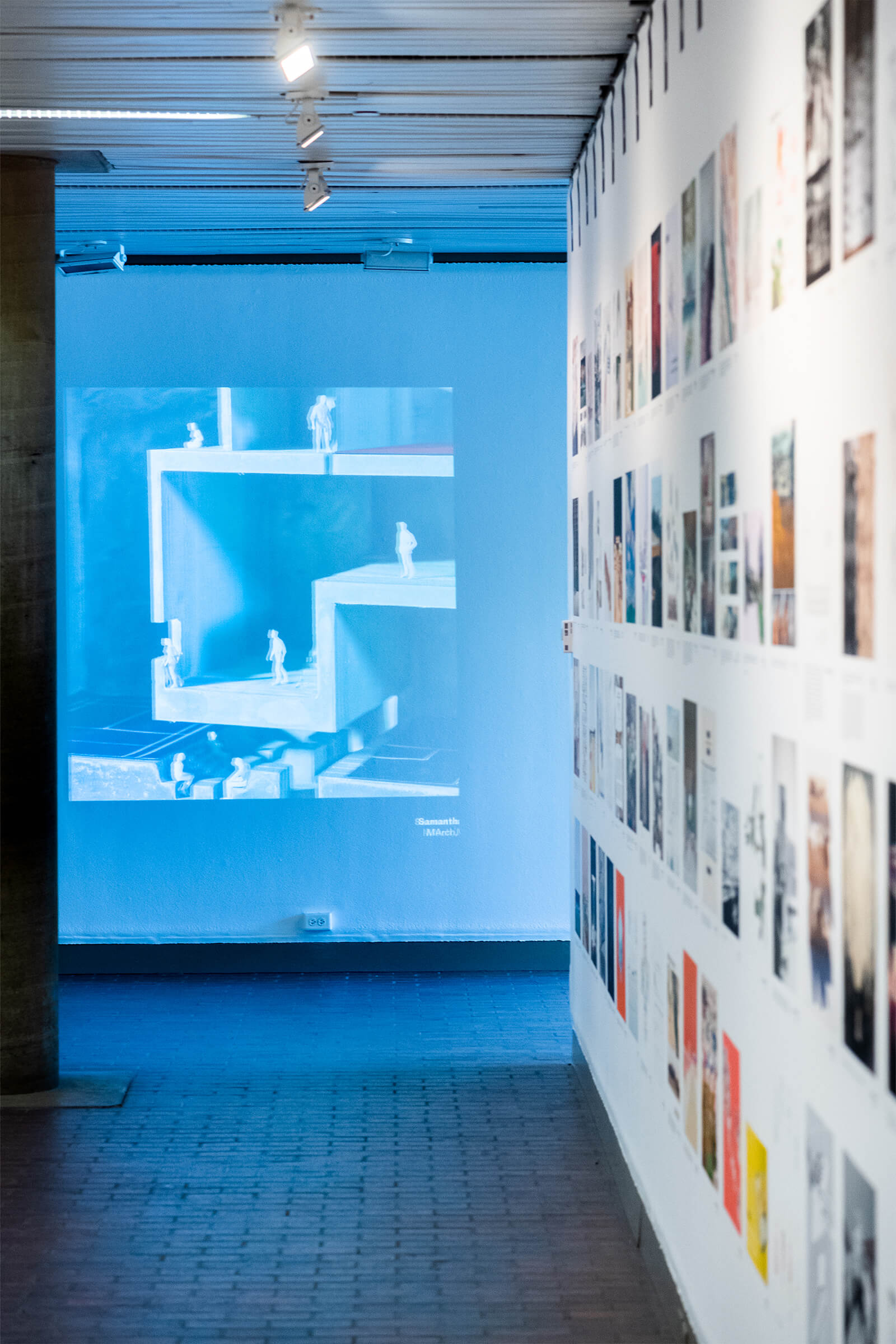 Gallery wall showing a collage of drawings and a projection at the end of the hallway.