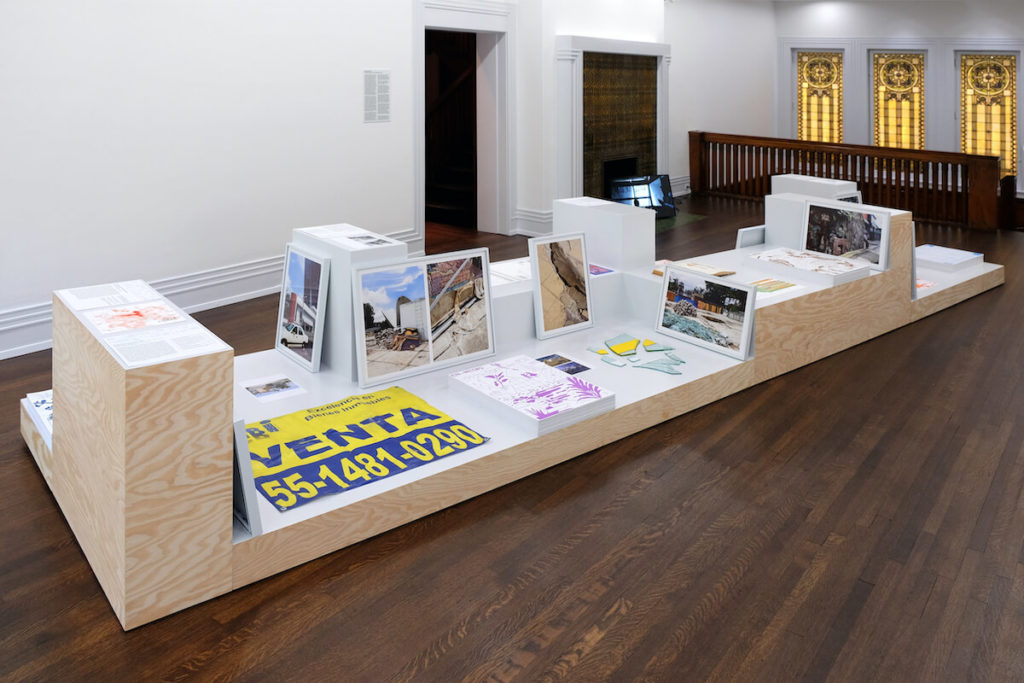 Gallery installation with objects on a wooden pedestal.