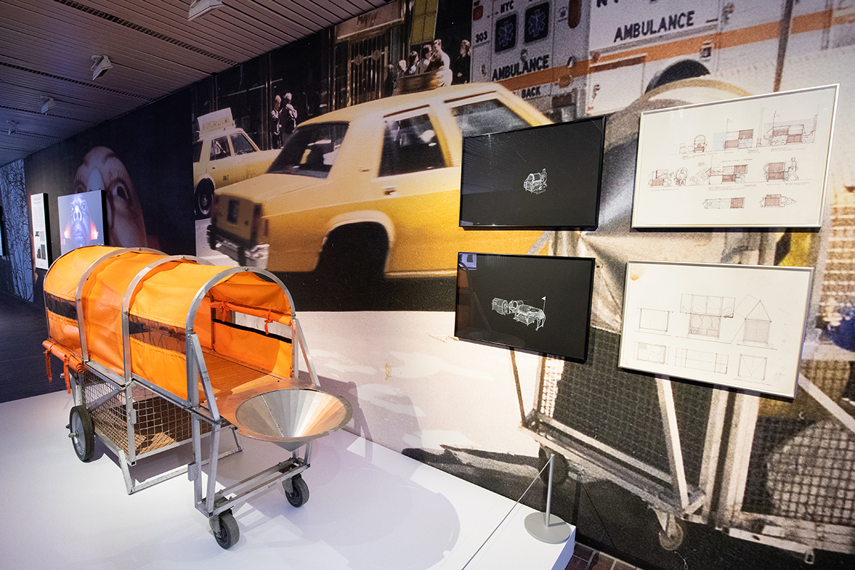 A display inside Druker Gallery showing Wodiczko’s “Homeless Vehicle”, a rolling cart made of metal and cloth. It includes a cargo area for belongings and is shown in its fully extended position which creates a sleeping area.
