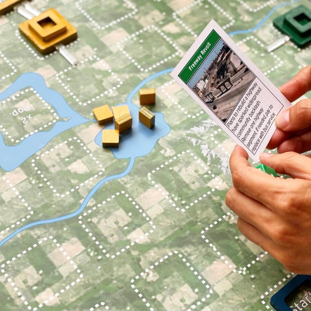 Hand hold card that reads Freeway Revolt above a gameboard.