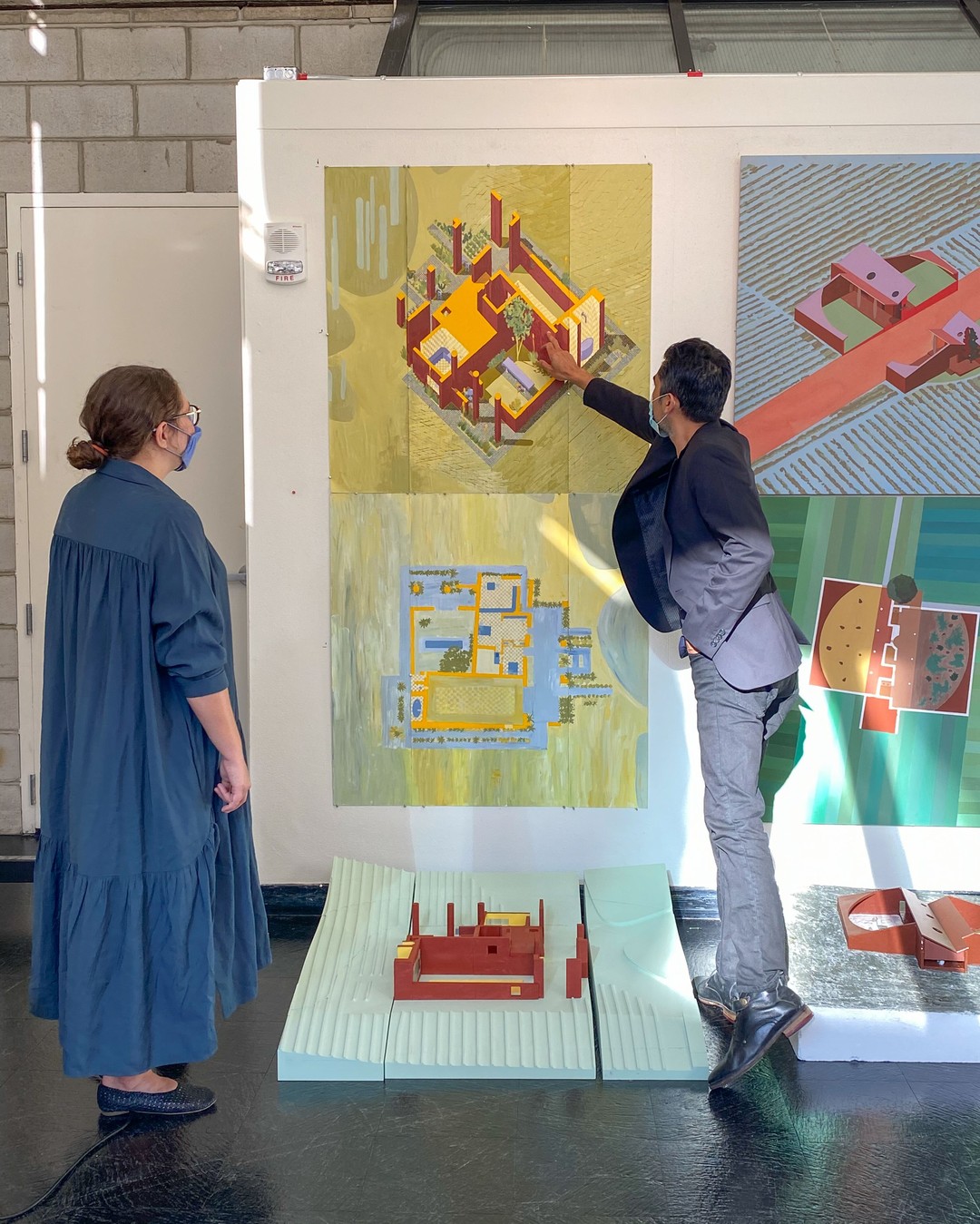 A faculty member points to an exhibited painting above a model as a student watches.