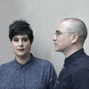 Headshot of two people. One has their head turned to the side and the other faces the camera.