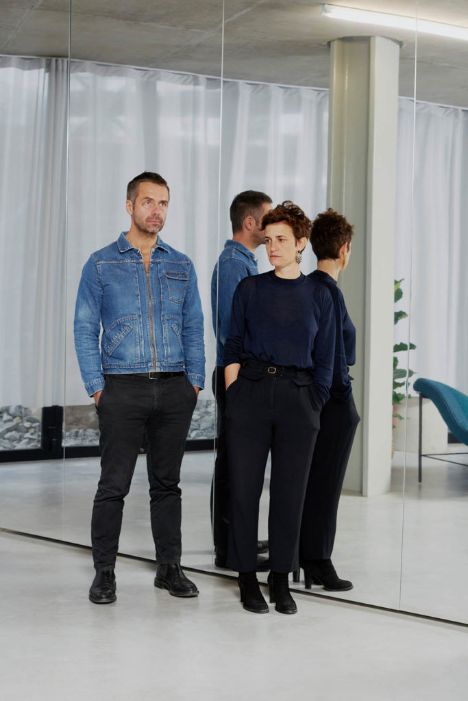 Stéphanie Bru and Alexandre Theriot stand next to each other in front of a mirrored wall.