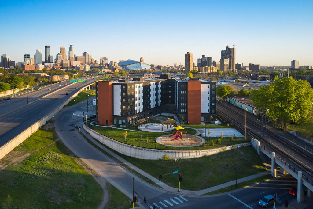 Aerial view of a housing complex near two large roads. A city with skyscrapers can be seen in the distance.