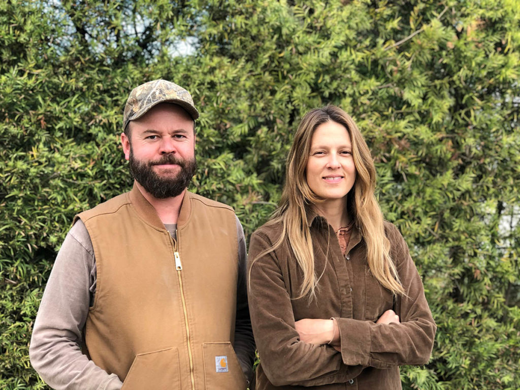 David Godshall and Jenny Jones stand next to each other in front of a lush green background.