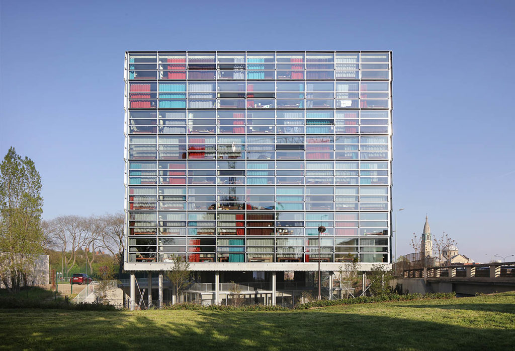 A building with large glass windows, with blue and red panels across some of them.