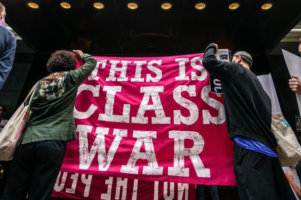 Two people hold up a pink and white sign that reads 