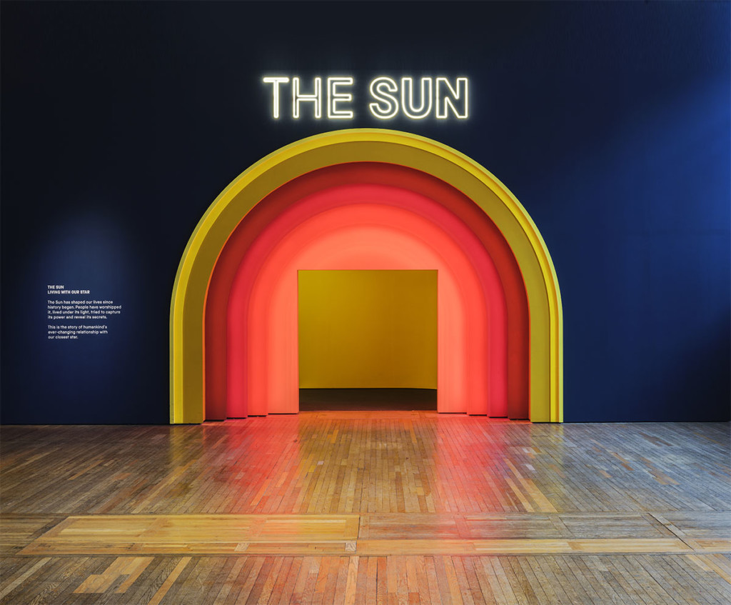 Blue wall with words "the sun" above yellow, red, and pink arch doorway in the wall 