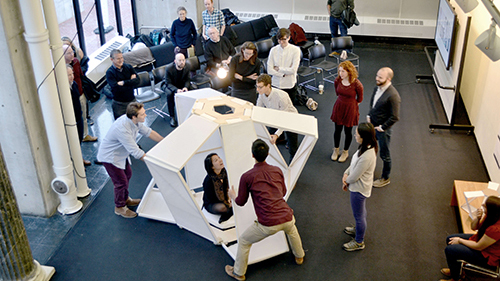 Group of students stand around a model during a review.