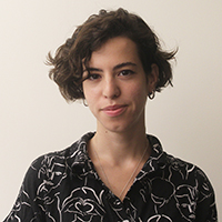 Headshot of Areti Kotsoni. Areti has a shaggy bob haircut, wears small hoop earrings and a black and white patterned blouse.