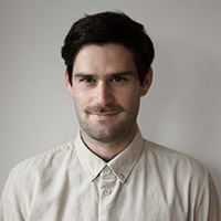 Headshot of Isaac Pollan. Isaac has short, dark hair and stubble, and wears an off-white button-down shirt.