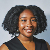 Headshot of Whytne Stevens. Whytne has curly dark hair and wears a sleeveless black blouse.