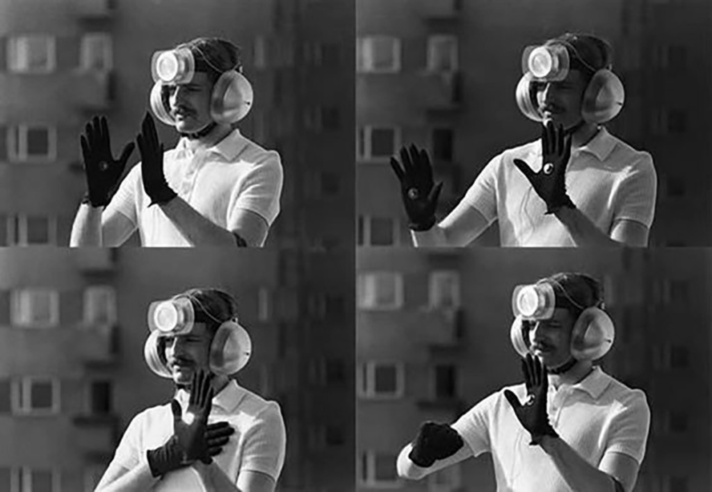 Four images of a man wearing an apparatus around his head and gloves on his hands, holding up his gloved hands in four different gestures.