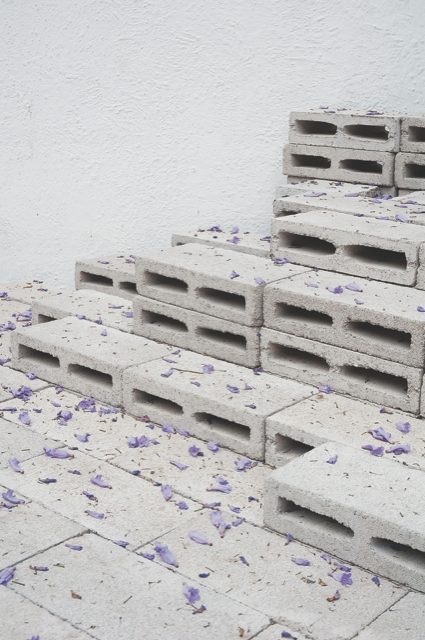 Concrete bricks organized in neat stacks. Purple flower petals are sprinkled over the grey material.