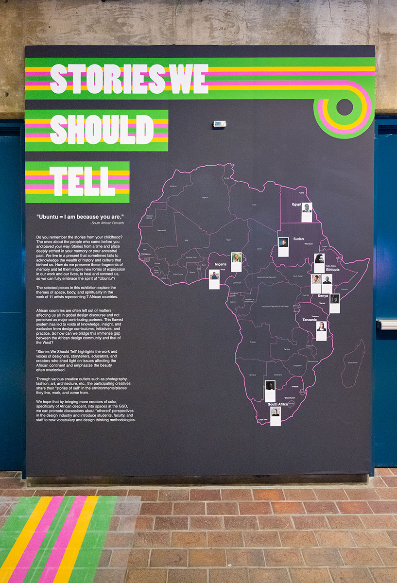A wall in Gund Hall showing the title “Stories We Should Tell” and a map of Africa with photos of individuals located in a variety of countries.