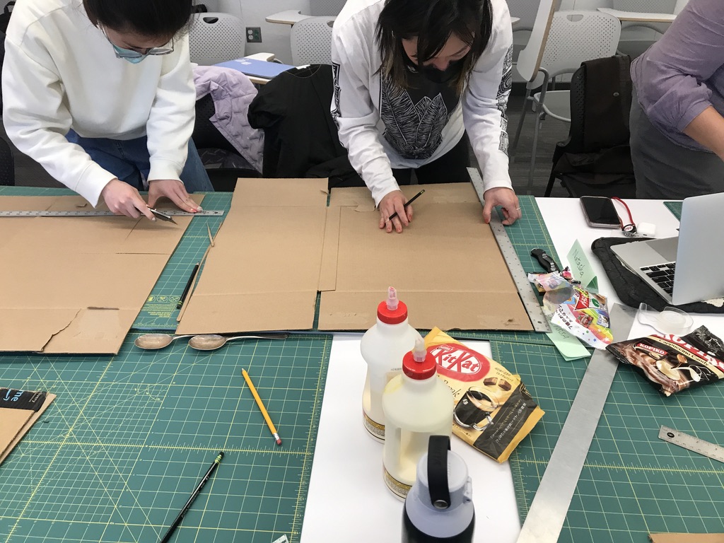 Students experiment with adaptive design cutting, using various tools with cardboard.