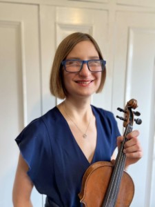 Violinist Julia LaGrand smiles at the camera holding a violin.