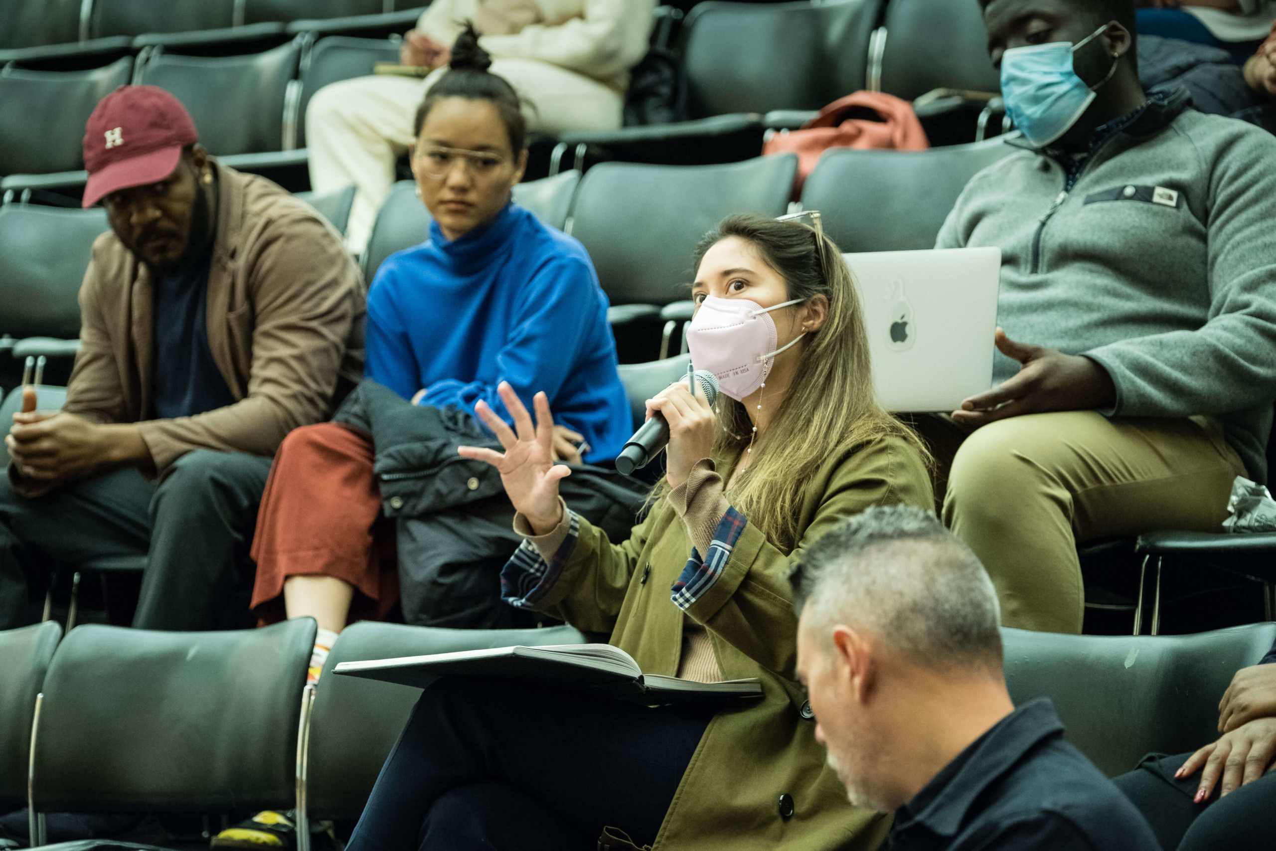 A masked audience member asks a question into a microphone.