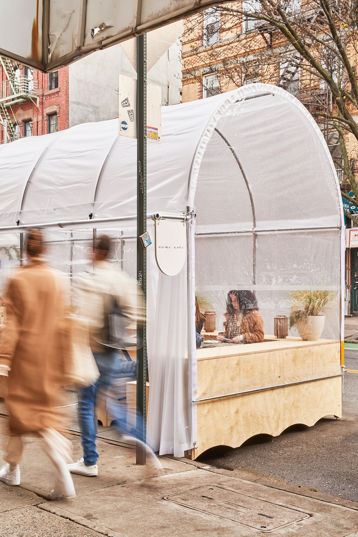 Re-ply structure in the street with people walking past and others inside enjoying a meal.