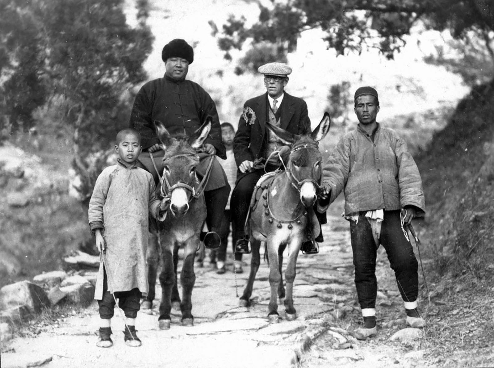 Black and white photo of 2 man on donkeys and a child with adult male next to them