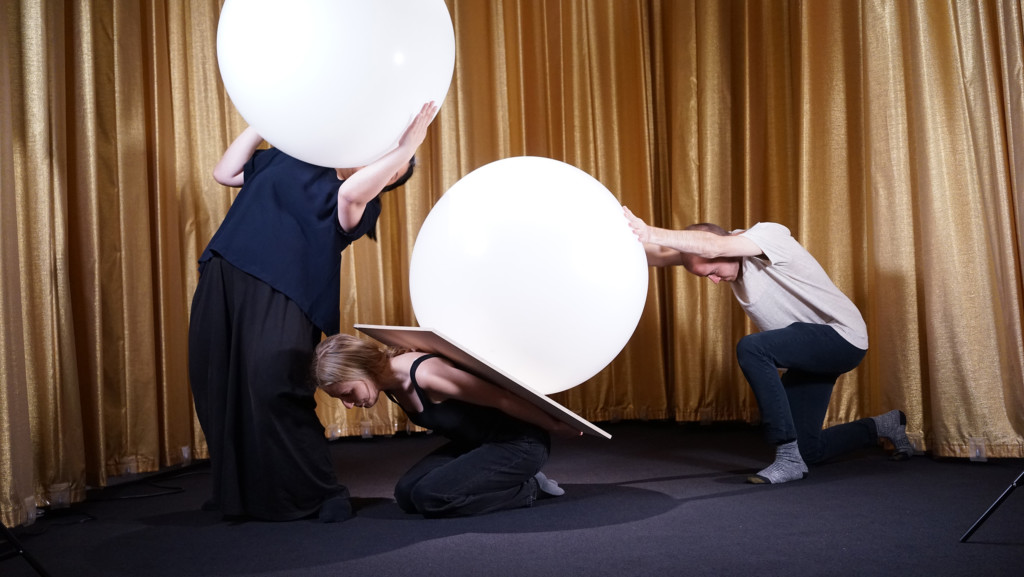 Three students performing dance with two large baloons