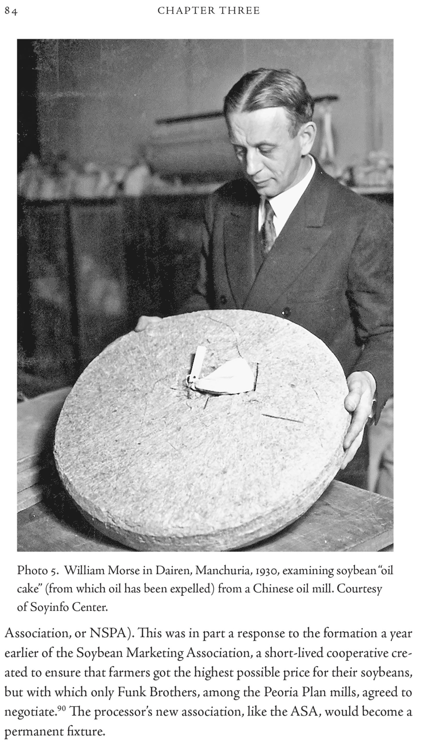 Black and white photo of a man examining soybean oil cake