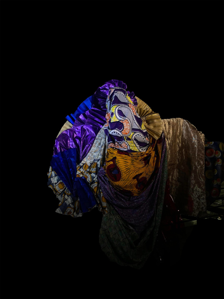 Artistic photo of a model make of colorful fabrics against a black background.