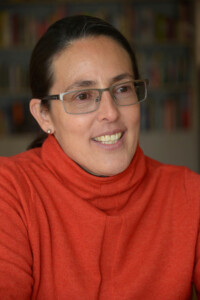Headshot of Ana Maria Duran Calisto, who wears a red-orange turtleneck shirt.