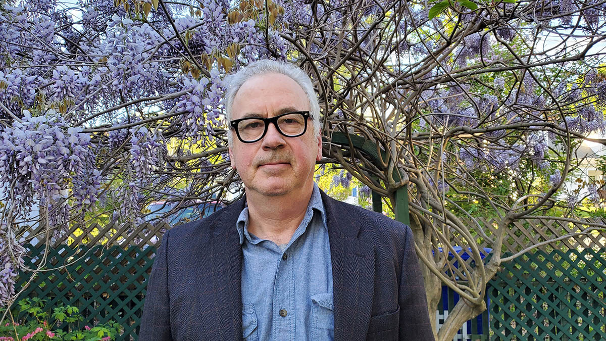 Headshot of Ethan Carr, who stands outdoors in front of a tree with purple flowers.