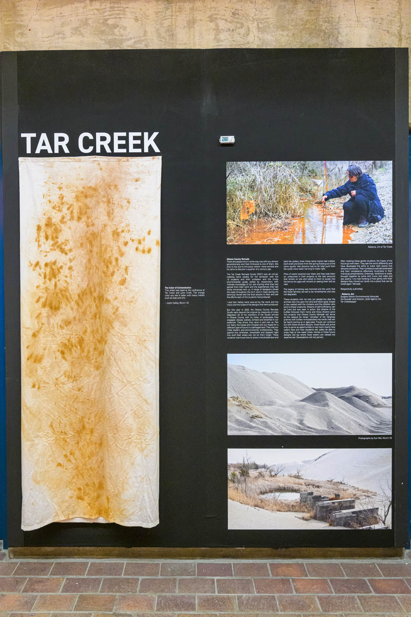 An exhibit wall showing text and photographs of an orange polluted river. A tall soiled cloth hangs next to them.