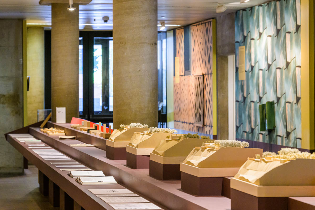 A view looking down the stepped side of a large shelf. On the shelf are models, books and text facsimiles. In the background is two full-scale murals of built facades.