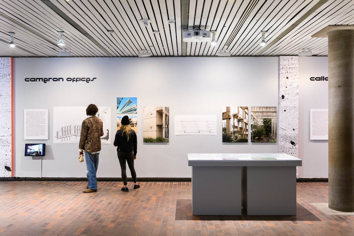 Two people looking at the work dipslayed on the wall. There is a display case next to them.