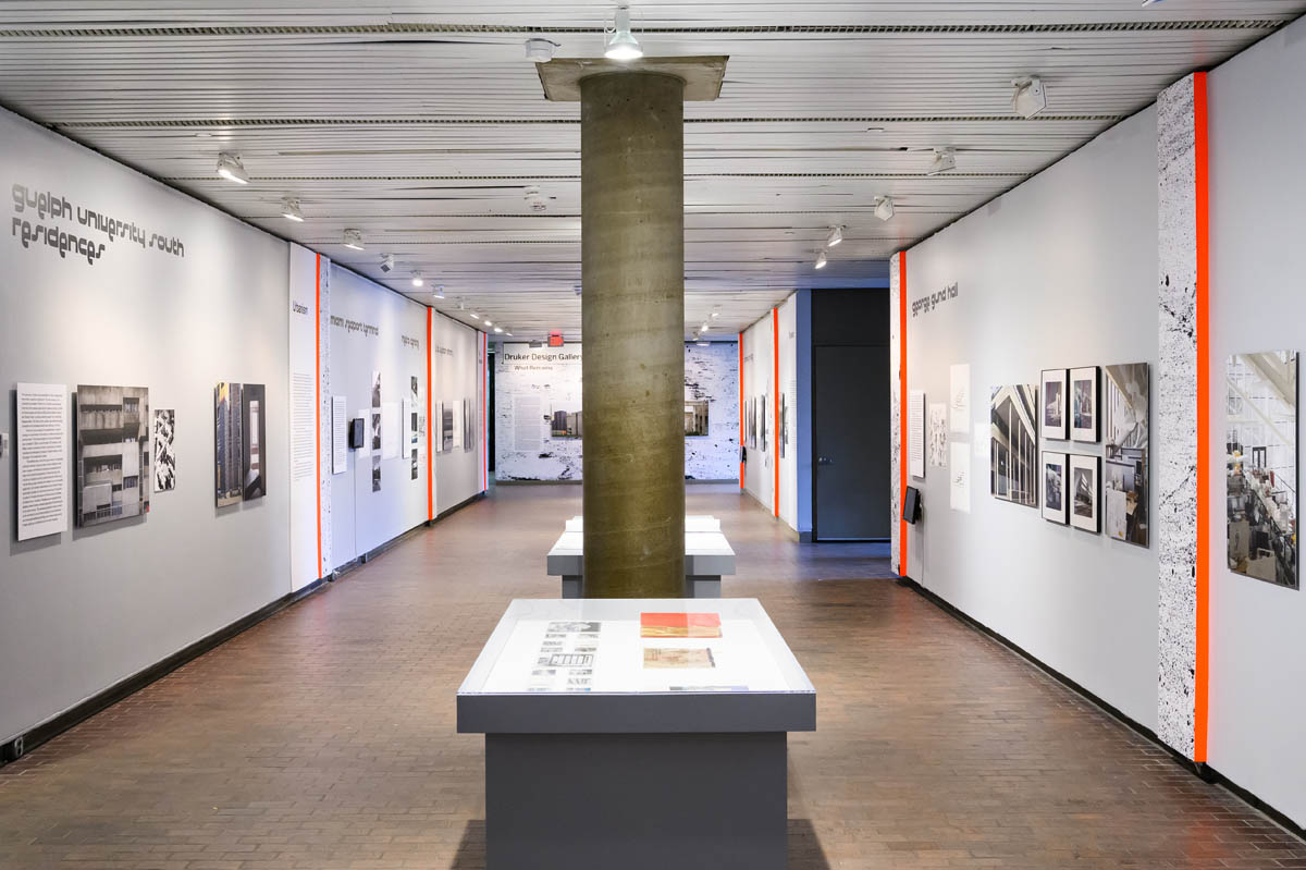 A long view down a cooridor of exhibition material. A series of display cases, are separated by a cment column.