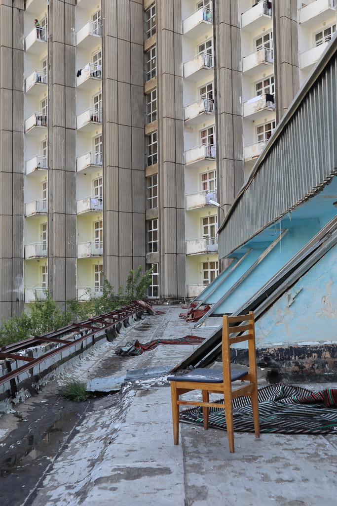 View of tall concrete building with lit up windows; brown chair and rubble in the foreground