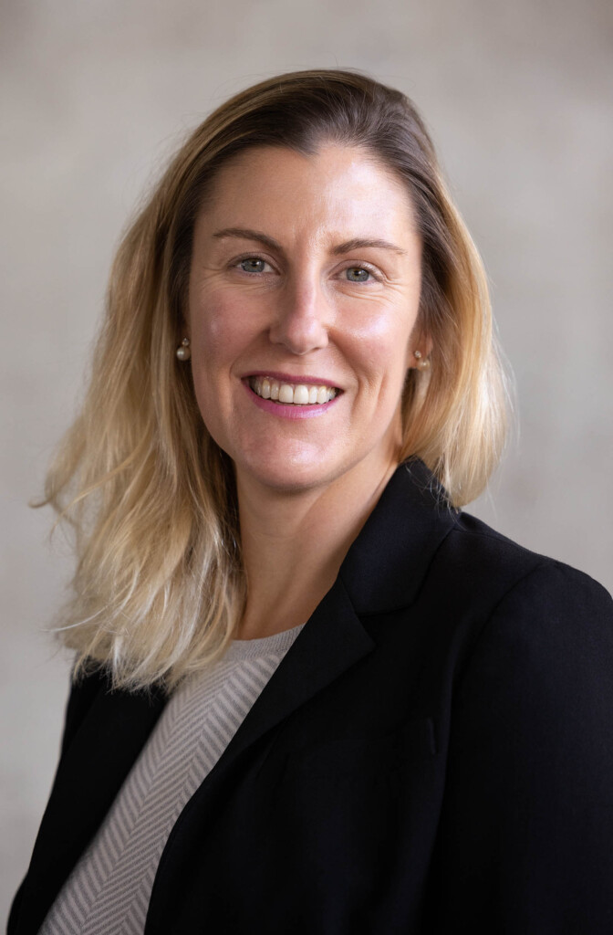 Headshot of caucasian female in black blazer, looking at the camera and smiling