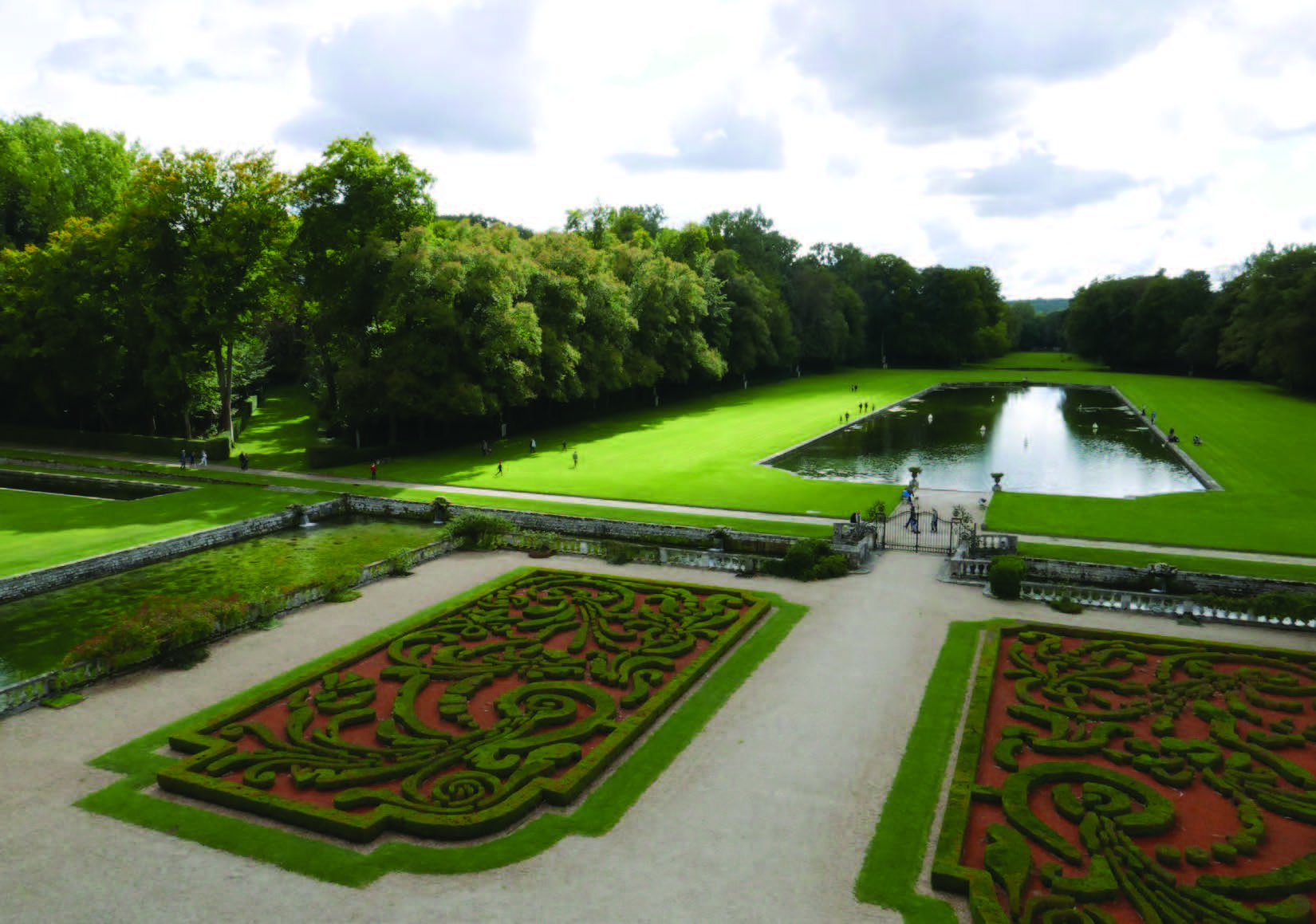 A landscape view of the lawn in front of the Courances Chateau, including a rectangular pond in the background and topiary bushes in an intricate pattern in the foreground.