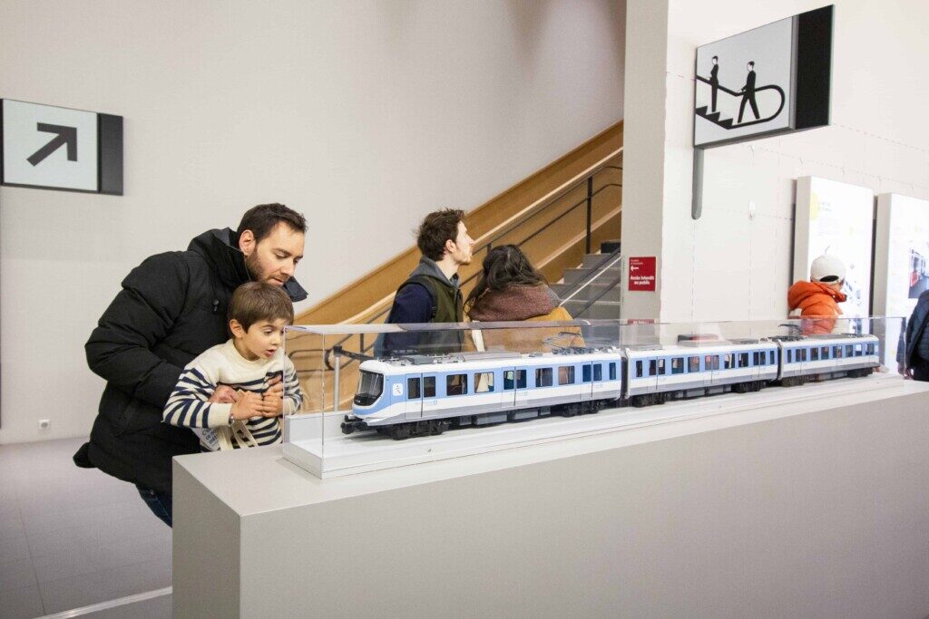 An adult lifts a child up to see a model of a train.