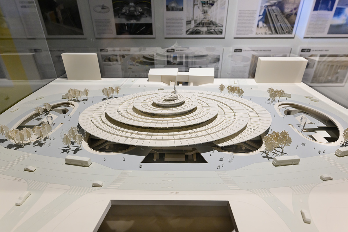 Architectural model of a train station with a spiral shaped roof, surrounded by a pedestrian plaza.