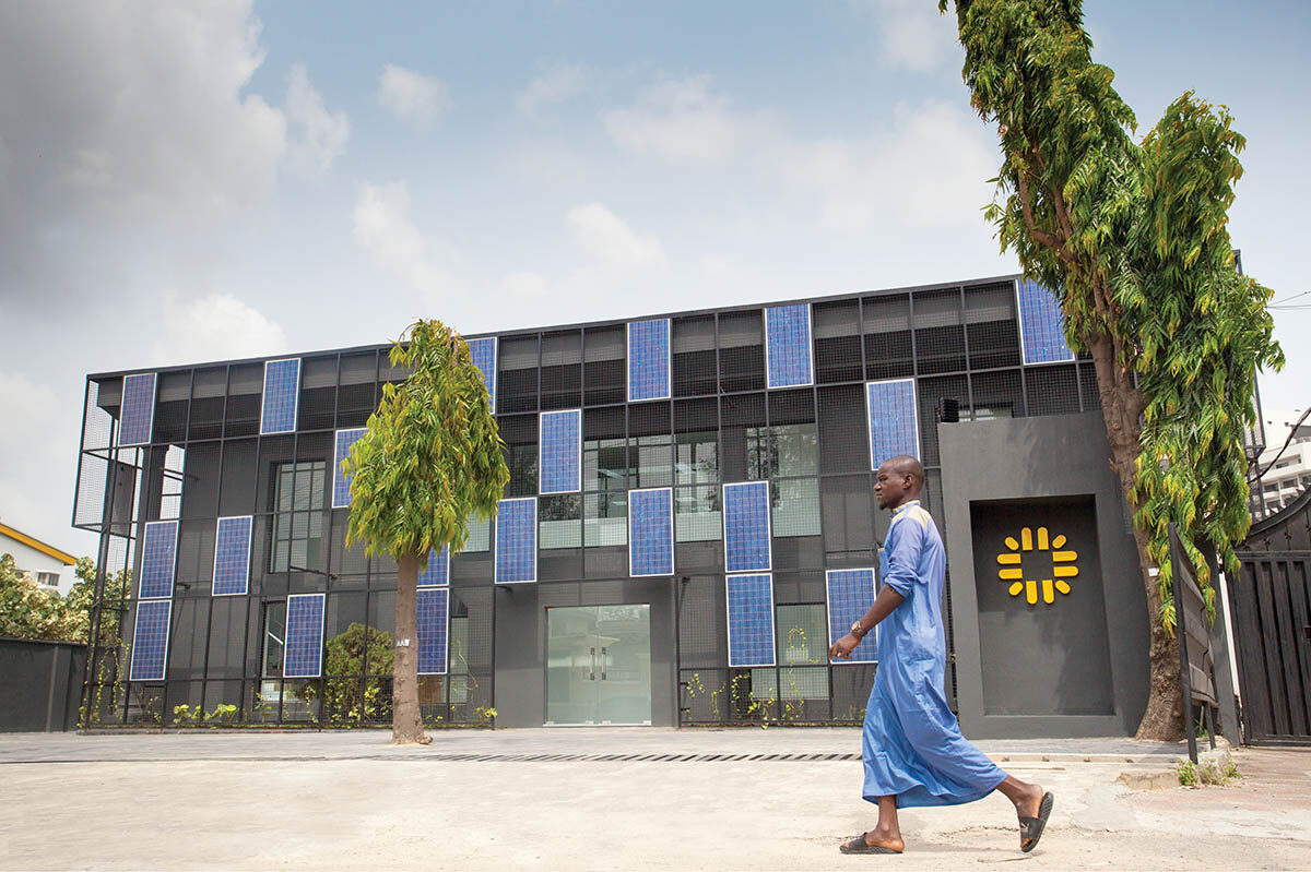 A gray building with a facade of solar panels is behind a person wearing blue.