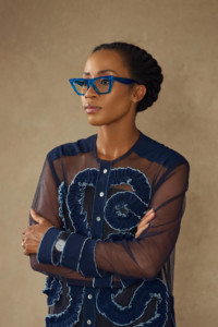 Headshot of Tosin Oshinowo, who wears a blue shirt and blue glasses.