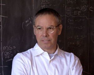 Headshot of Stan Allen, who wears a white shirt and glasses. He stands in front of a chalkboard with writing on it.
