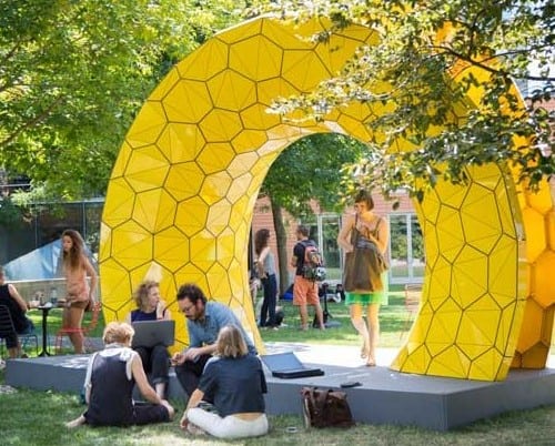 Students walk sit around a yellow sculpture in the Gund Back Yard.