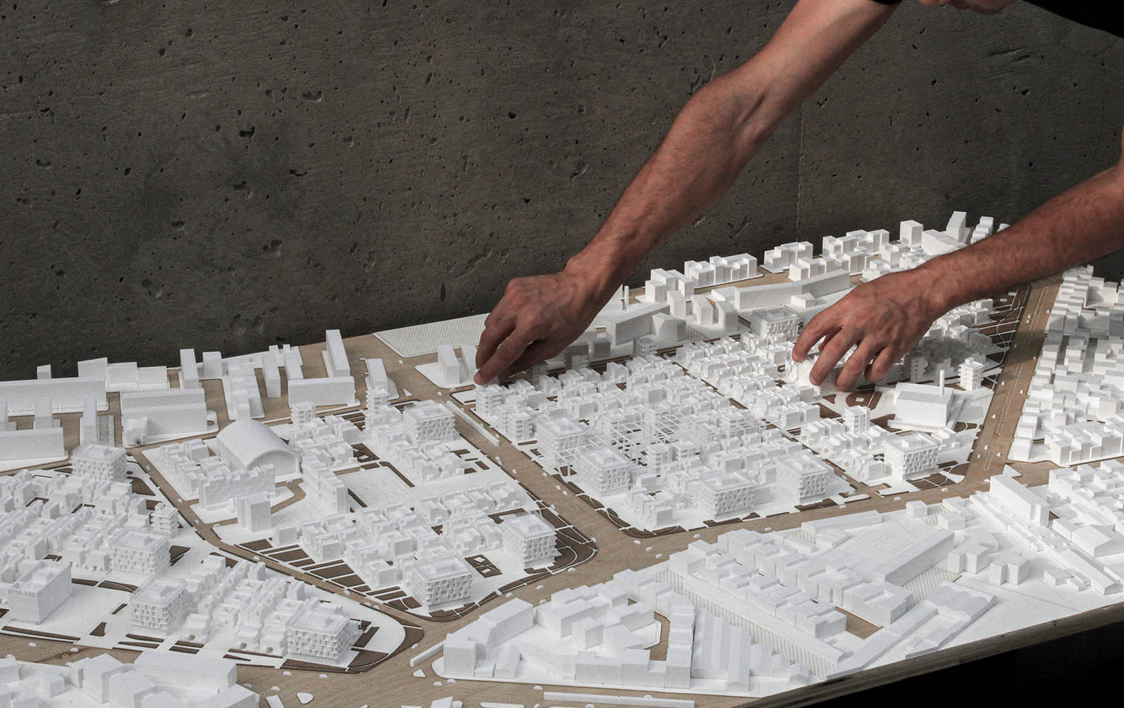 A photo of a physical model of a city with person's hands touching the model on the right side.
