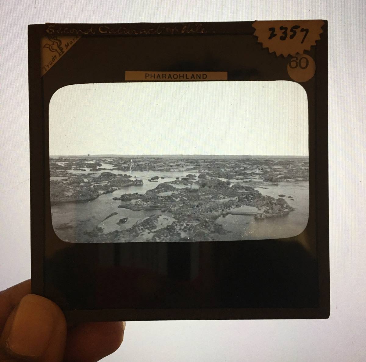 A hand holds a glass slide showing a landscape: the second cataract of the Nile.
