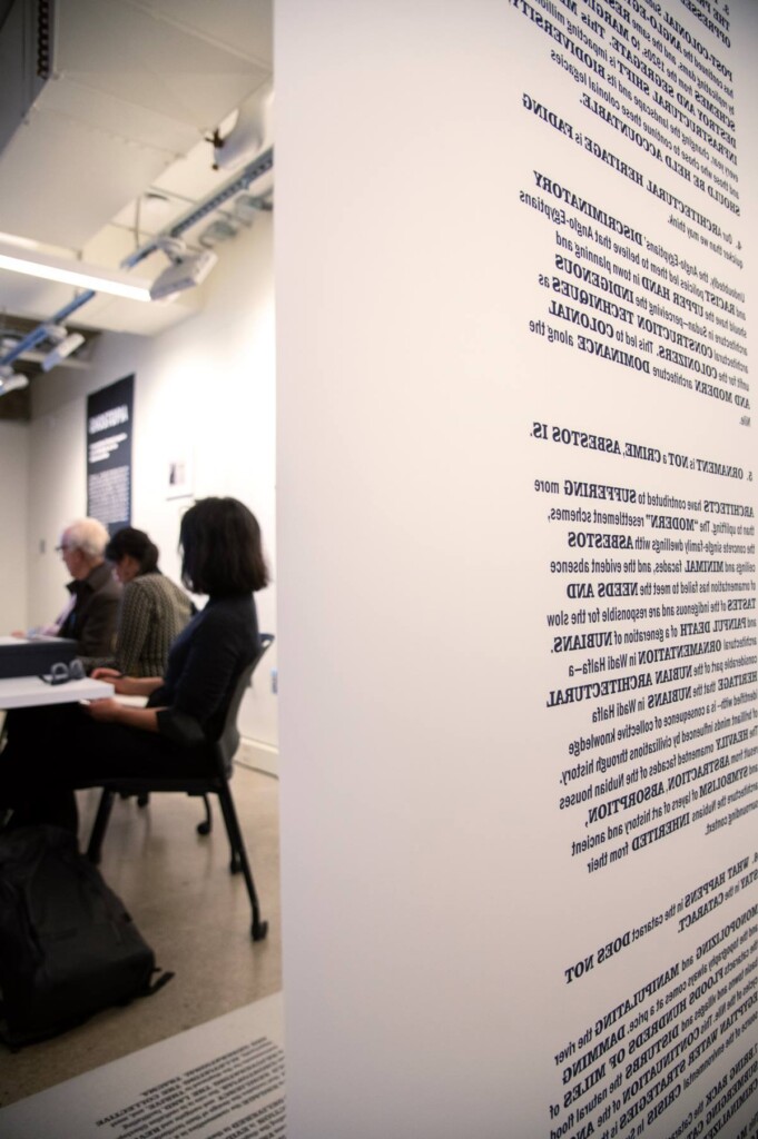 A view from behind of a banner with several paragraphs of text (unreadable, backwards). Beyond this, people are sitting at a table.