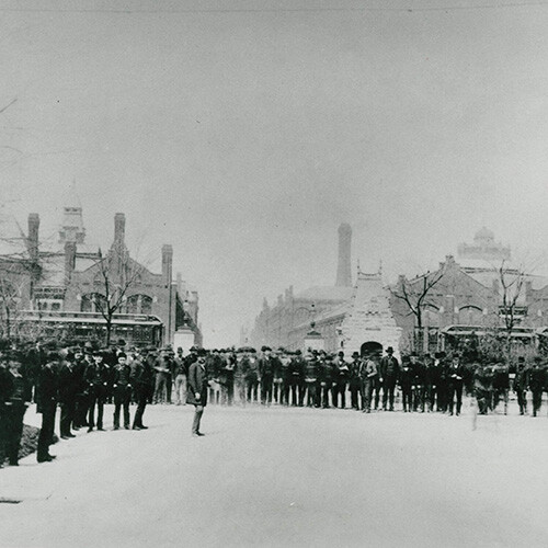 A black-and-white image of a crowd on a historical streetscape.
