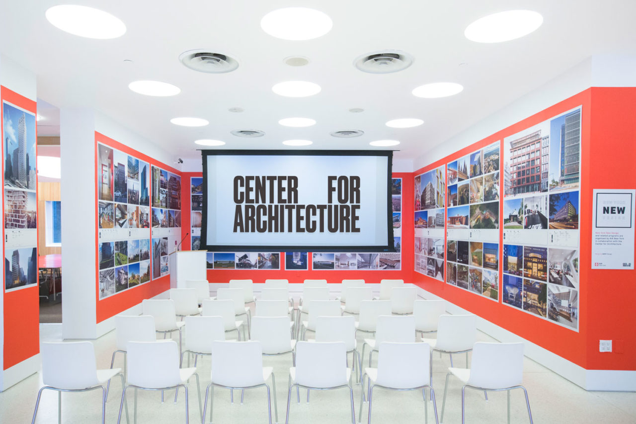 Center for Architecture screening space with red/orange walls and empty white chairs