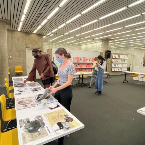 Two women stand over a table at the Loeb Library that is covered with documents.